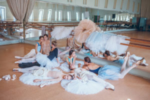 Thr seven ballerinas sitting and lying against ballet rack in the rehearsal hall of the theater